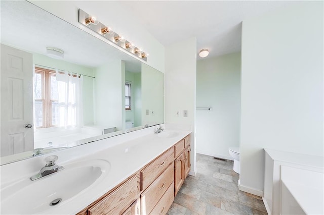 full bath featuring baseboards, a sink, toilet, and double vanity