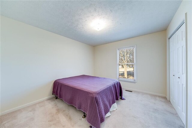 bedroom featuring light carpet, a closet, a textured ceiling, and baseboards