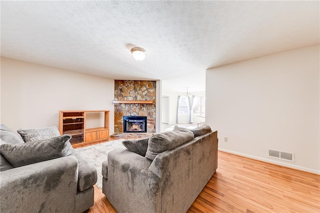 living area with baseboards, visible vents, a textured ceiling, a stone fireplace, and light wood-style floors