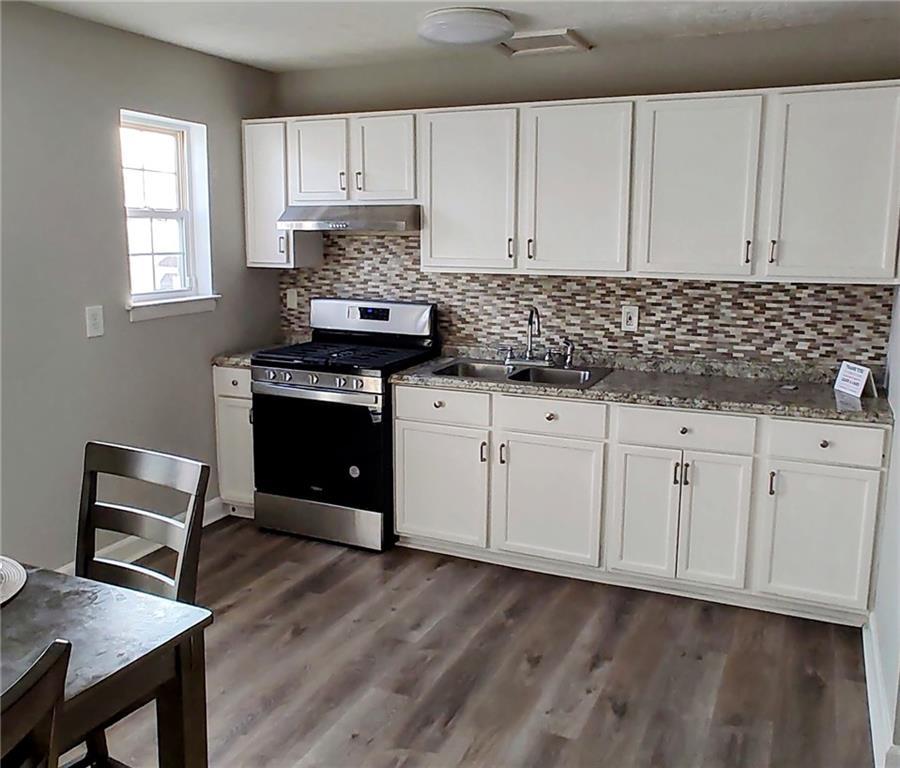 kitchen with sink, dark wood-type flooring, backsplash, gas stove, and white cabinets