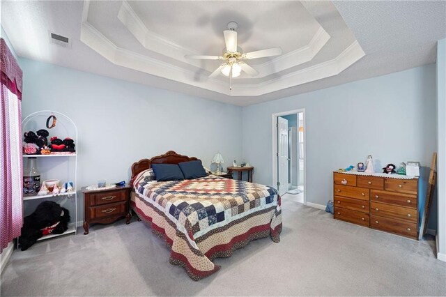 carpeted bedroom featuring ensuite bathroom, a raised ceiling, ceiling fan, and ornamental molding