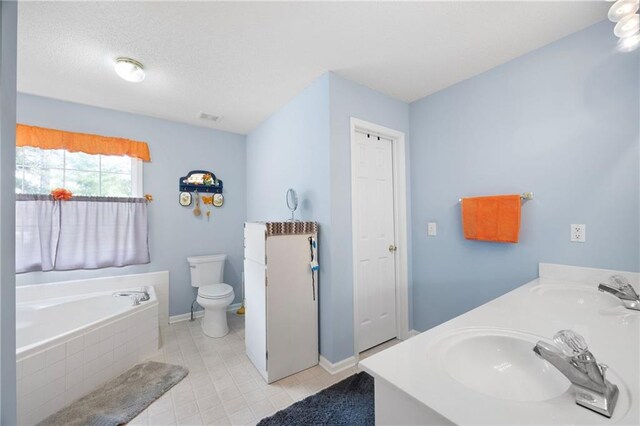 bathroom with a textured ceiling, vanity, tile patterned flooring, tiled bath, and toilet