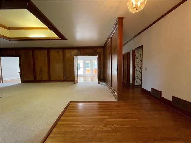 unfurnished living room with a notable chandelier, crown molding, wooden walls, and hardwood / wood-style flooring