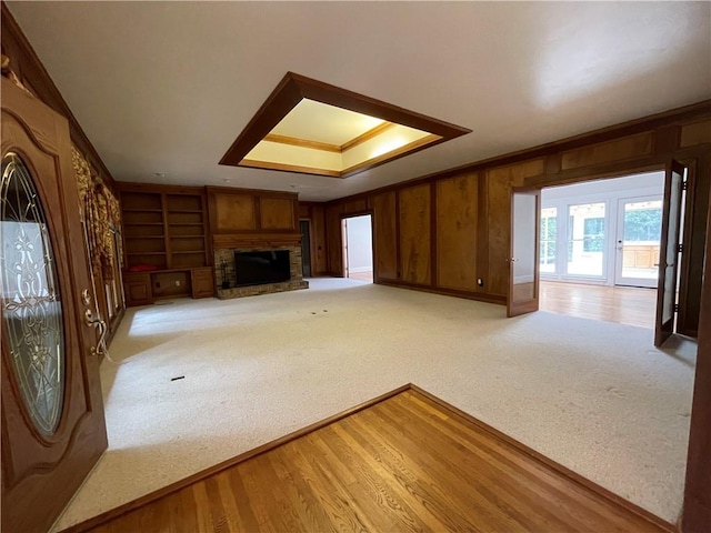 unfurnished living room featuring built in shelves, wooden walls, light wood-type flooring, and crown molding