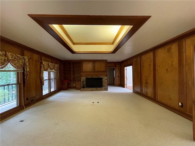 unfurnished living room with wooden walls, a fireplace, a tray ceiling, and light carpet