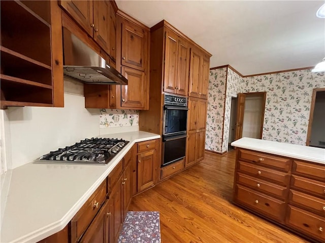 kitchen featuring hanging light fixtures, light hardwood / wood-style floors, stainless steel gas cooktop, ornamental molding, and double oven