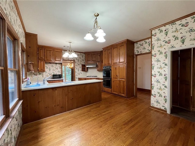 kitchen featuring light wood-type flooring, a notable chandelier, kitchen peninsula, hanging light fixtures, and crown molding