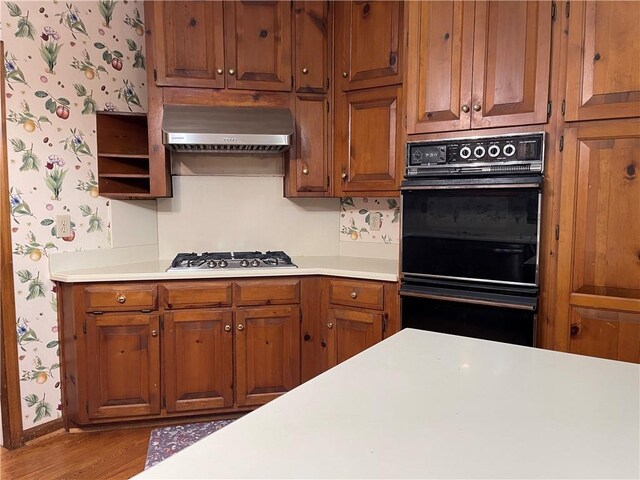 kitchen featuring stainless steel gas stovetop, double oven, light hardwood / wood-style flooring, and ventilation hood