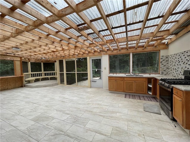 kitchen with light stone counters, tasteful backsplash, stainless steel gas range oven, a skylight, and sink