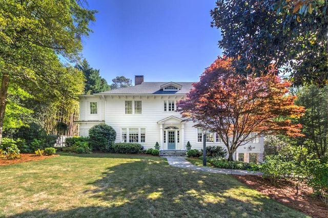 colonial inspired home featuring a chimney and a front lawn