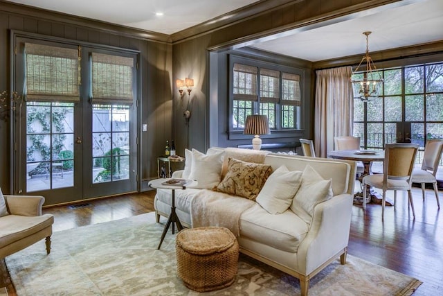 living area with crown molding, an inviting chandelier, visible vents, wood finished floors, and french doors