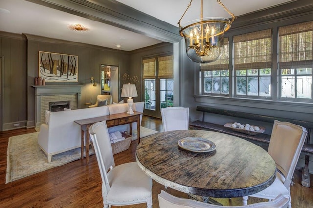 dining space featuring an inviting chandelier, a brick fireplace, ornamental molding, and wood finished floors