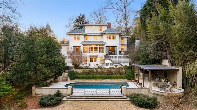 back of property with stairs, a patio, a chimney, and an outdoor pool