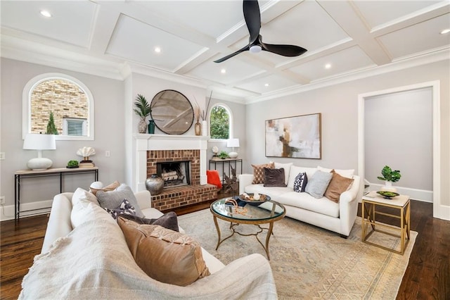 living room with coffered ceiling, crown molding, ceiling fan, dark wood-type flooring, and a brick fireplace