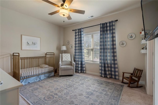 carpeted bedroom with baseboards, a crib, a ceiling fan, and visible vents