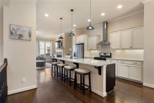 kitchen featuring wall chimney range hood, appliances with stainless steel finishes, ornamental molding, and a breakfast bar