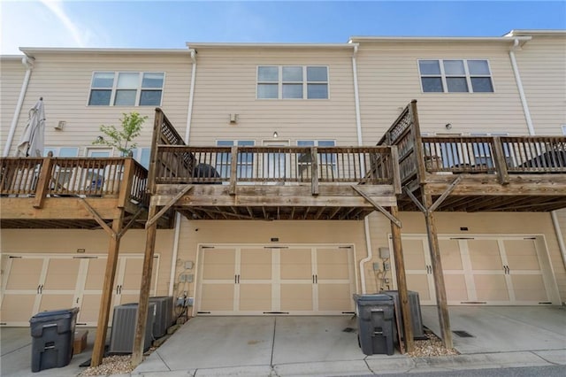 back of house with concrete driveway, a wooden deck, an attached garage, and cooling unit