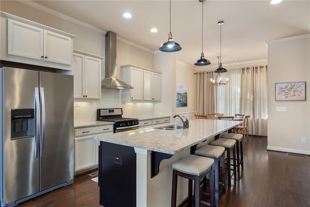 kitchen featuring crown molding, appliances with stainless steel finishes, a sink, an island with sink, and wall chimney exhaust hood