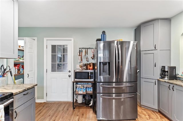 kitchen with stainless steel appliances, light stone countertops, gray cabinetry, and light wood-type flooring