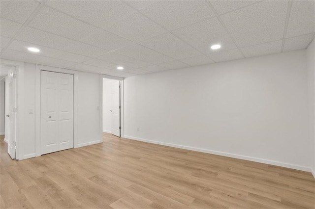 basement with a paneled ceiling and light wood-type flooring