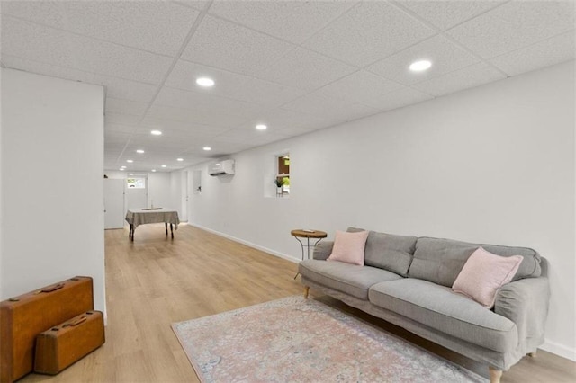 living room with a wall mounted air conditioner, light wood-type flooring, and a drop ceiling