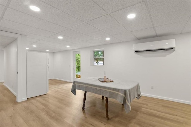 interior space with a drop ceiling, a wall mounted air conditioner, and light wood-type flooring