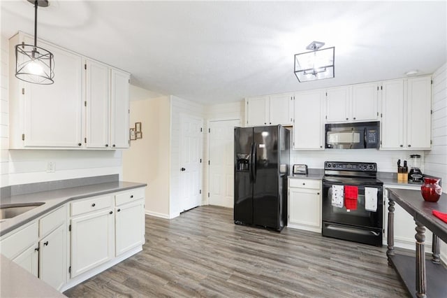 kitchen with white cabinets, wood finished floors, black appliances, and decorative light fixtures