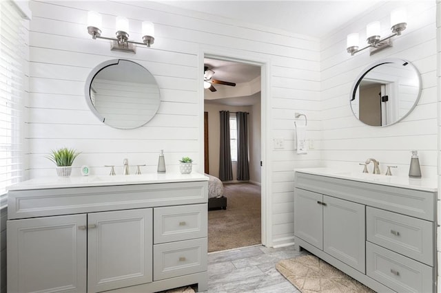bathroom with a sink, a ceiling fan, wood walls, and two vanities