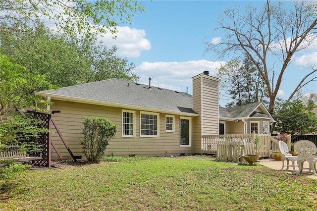 back of house with roof with shingles, a deck, crawl space, a chimney, and a lawn