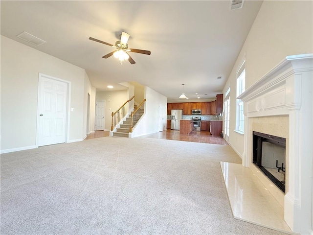 unfurnished living room with ceiling fan, light colored carpet, and a fireplace