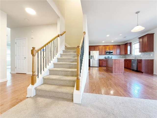 interior space featuring appliances with stainless steel finishes, a center island, wood-type flooring, decorative backsplash, and decorative light fixtures