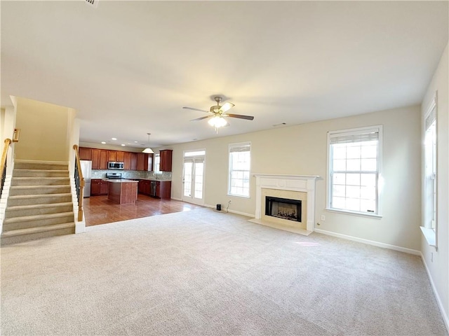 unfurnished living room featuring ceiling fan, a healthy amount of sunlight, and light carpet