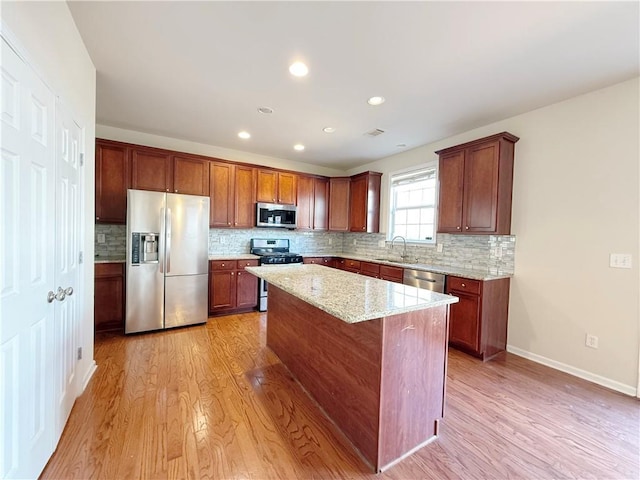 kitchen featuring sink, stainless steel appliances, light stone countertops, a kitchen island, and light wood-type flooring