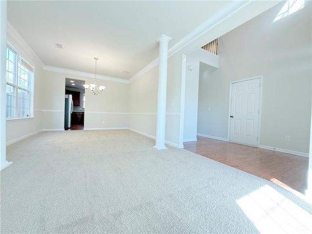 carpeted empty room featuring ornate columns, crown molding, and an inviting chandelier