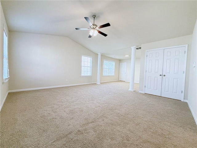 empty room featuring vaulted ceiling, decorative columns, ceiling fan, and carpet