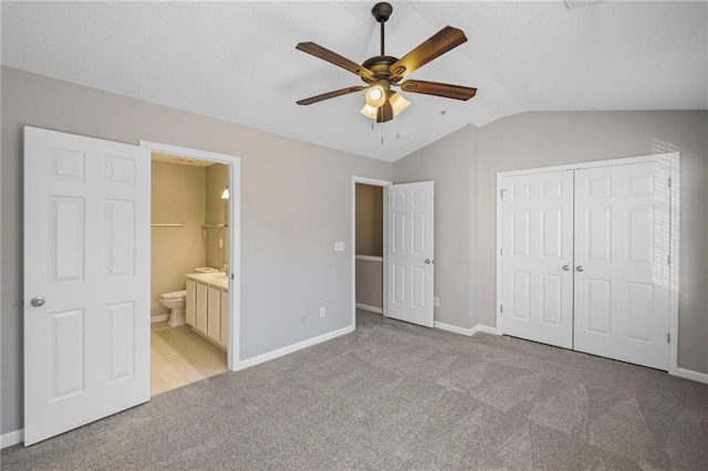 unfurnished bedroom featuring ensuite bath, a closet, carpet floors, baseboards, and vaulted ceiling