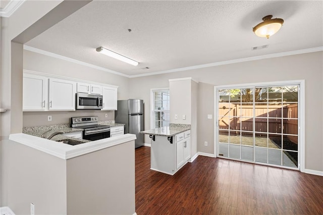 kitchen featuring visible vents, dark wood finished floors, a peninsula, a sink, and stainless steel appliances