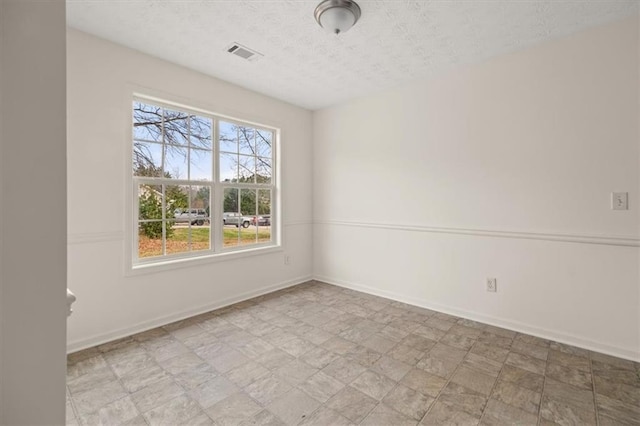 empty room with visible vents, light floors, a textured ceiling, and baseboards