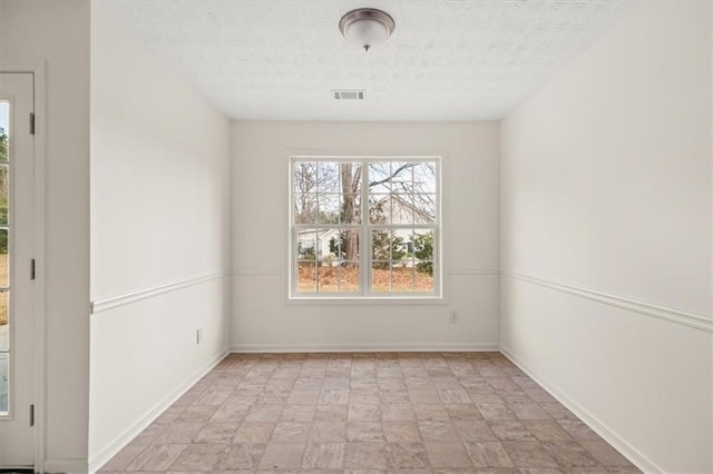 empty room with visible vents, a textured ceiling, and baseboards