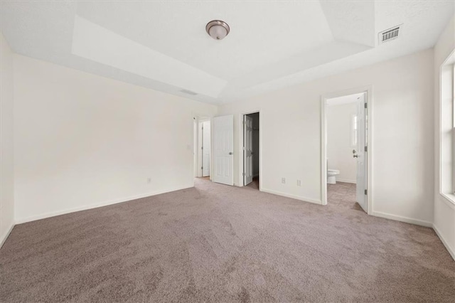 unfurnished bedroom with a raised ceiling, baseboards, visible vents, and carpet floors