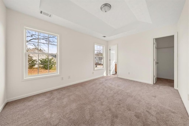 unfurnished bedroom featuring visible vents, multiple windows, a raised ceiling, and carpet