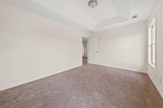 spare room featuring a tray ceiling, baseboards, visible vents, and carpet floors