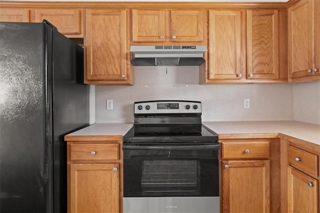 kitchen with electric range, freestanding refrigerator, light countertops, under cabinet range hood, and brown cabinets