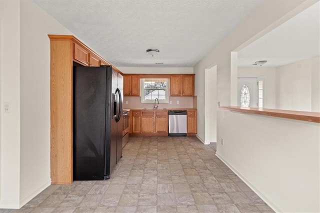 kitchen featuring baseboards, a sink, light countertops, dishwasher, and black fridge