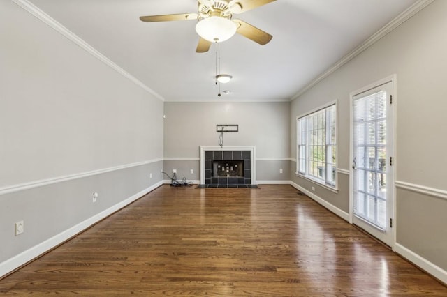 unfurnished living room featuring a tiled fireplace, crown molding, dark wood-type flooring, and ceiling fan