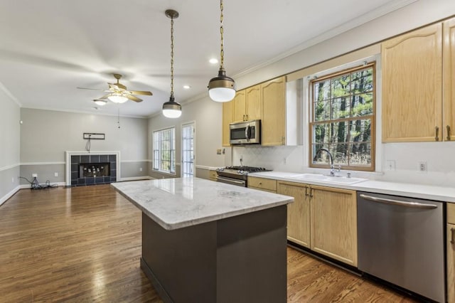 kitchen with sink, crown molding, stainless steel appliances, a tiled fireplace, and light brown cabinets