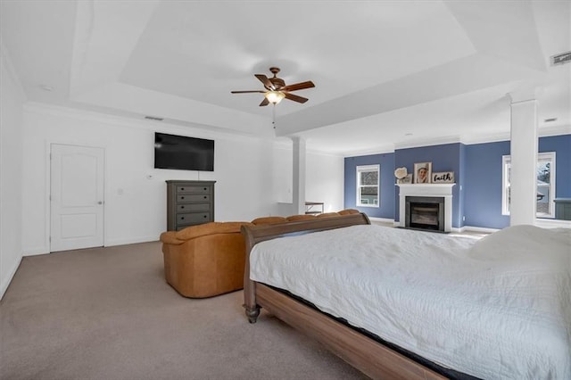 carpeted bedroom featuring a tray ceiling, a glass covered fireplace, a ceiling fan, and baseboards
