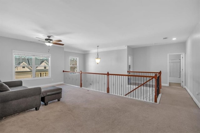 sitting room featuring carpet flooring, ceiling fan, baseboards, an upstairs landing, and crown molding