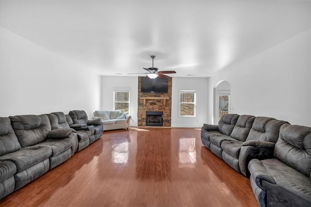 living area featuring arched walkways, wood finished floors, a ceiling fan, and a stone fireplace