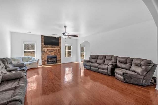 living area with arched walkways, a stone fireplace, wood finished floors, and ceiling fan